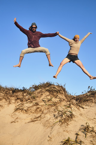 Portugal, Algarve, Paar am Strand springt die Düne hinunter, lizenzfreies Stockfoto