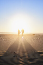 Portugal, Algarve, Paar mit Hund bei Sonnenuntergang am Strand - JRF00340