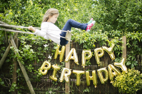 Dekoration für Geburtstagsfeier im Garten mit goldenen Luftballons und schwingenden Mädchen im Vordergrund - MOEF00133