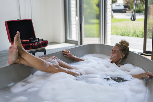 Mature woman taking bubble bath, listening music from analogue record player - RIBF00675