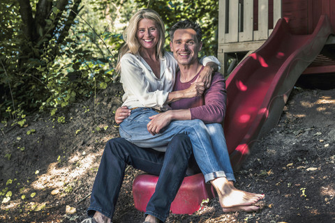 Glückliches Paar sitzt auf der Rutsche eines Gartenhauses im Wald, lizenzfreies Stockfoto