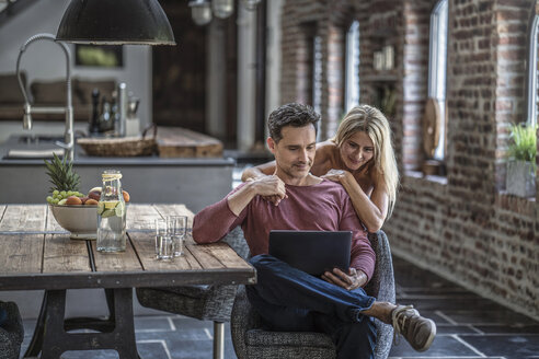 Glückliches Paar sitzt in der Küche eines Landhauses und schaut auf einen Laptop - RIBF00687