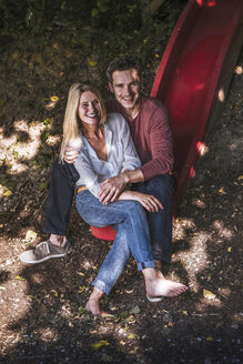 Glückliches Paar sitzt auf einer Rutsche im Wald - RIBF00693