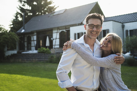 Ein glückliches Paar umarmt sich im Garten seines Landhauses, lizenzfreies Stockfoto