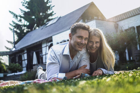 Happy couple lying on grass in the garden of their country house - RIBF00711