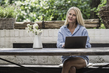 Ältere Frau sitzt auf der Terrasse und benutzt einen Laptop - RIBF00712