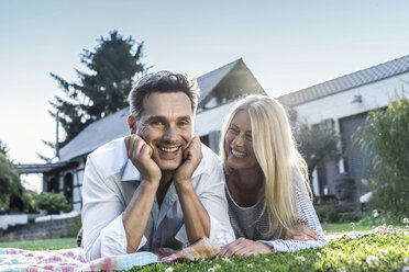 Ein glückliches Paar liegt im Garten seines Landhauses im Gras - RIBF00717
