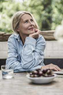 Ältere Frau sitzt auf der Terrasse, mit Kirschen auf dem Tisch - RIBF00727