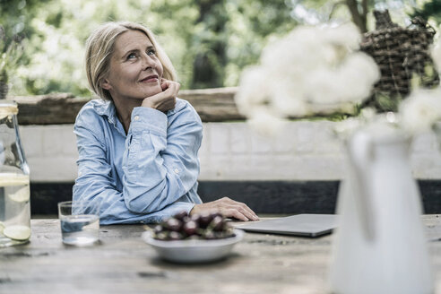 Ältere Frau sitzt auf der Terrasse, mit Kirschen auf dem Tisch - RIBF00728