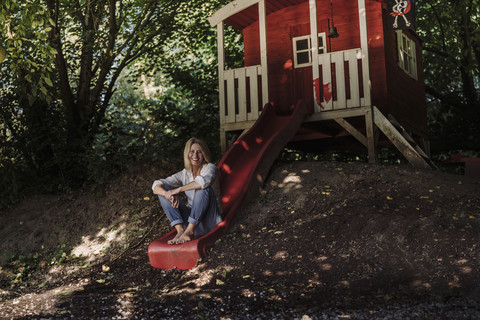 Reife Frau sitzt auf einer Rutsche vor einem Gartenhaus im Wald, lizenzfreies Stockfoto