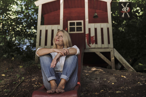 Reife Frau sitzt auf einer Rutsche vor einem Gartenhaus im Wald, lizenzfreies Stockfoto