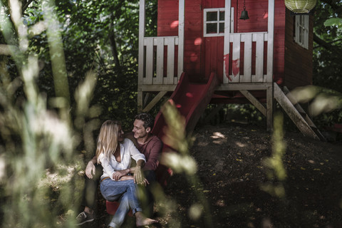 Happy couple sitting on slide of garden shed in the woods stock photo