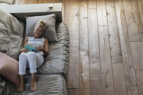 Frau entspannt sich auf der Couch und liest ein Buch - RIBF00756