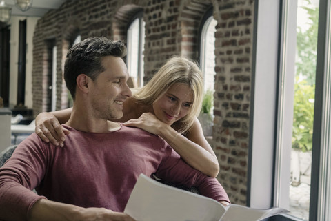 Happy couple siting in country house kitchen, reading newspaper stock photo