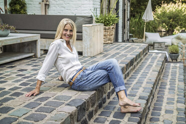 Ältere Frau sitzt auf der Treppe ihrer Gartenterrasse - RIBF00765