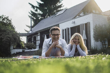 Happy couple lying on grass in the garden of their country house - RIBF00767