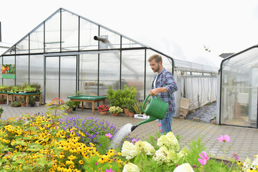 Gärtner gießt Blumen vor einem Gewächshaus - LYF00795