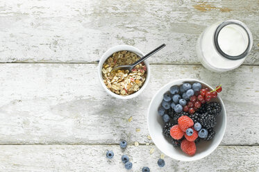 Bowl of granola, milk bottle and bowl of berries on wood - ASF06105
