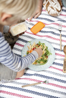Junge verteilt geriebenen Käse auf Nudelsalat bei einem Picknick im Wald - MFRF00982
