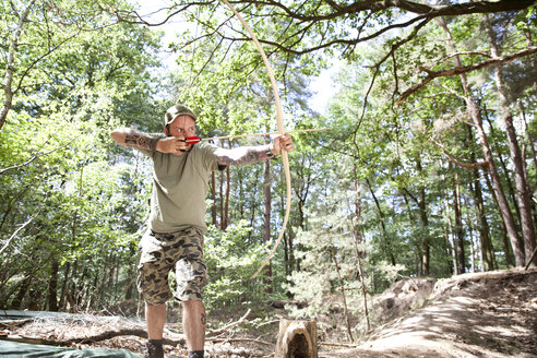 Mann schießt mit Pfeil und Bogen im Wald - MFRF00983