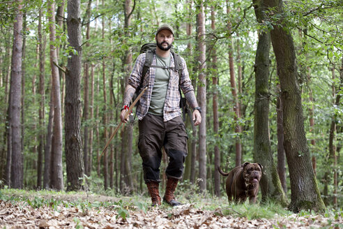 Mann mit Pfeil und Bogen geht mit Hund im Wald spazieren - MFRF01011