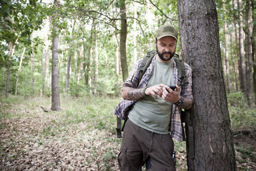 Mann mit Rucksack auf einer Wanderung im Wald mit Mobiltelefon - MFRF01018