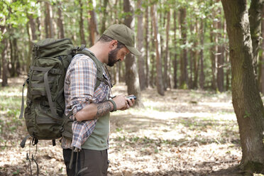 Man with backpack on a hiking trip in forest using cell phone - MFRF01019