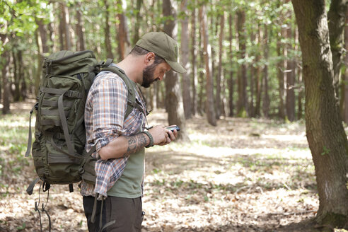 Mann mit Rucksack auf einer Wanderung im Wald mit Mobiltelefon - MFRF01019