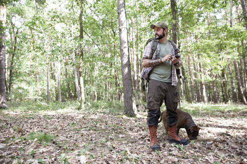 Mann mit Hund beim Wandern im Wald, der ein Mobiltelefon benutzt - MFRF01020