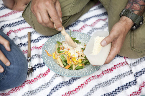 Mann, der bei einem Picknick geriebenen Käse auf Nudelsalat streut - MFRF01039