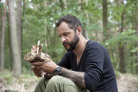 Mann schaut auf geschnitztes Holzboot im Wald, lizenzfreies Stockfoto