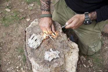 Ein Mann entzündet ein Feuer auf einem Baumstumpf im Wald - MFRF01047