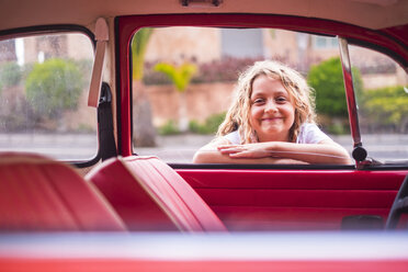 Porträt eines lächelnden blonden Mädchens, das sich an ein Autofenster lehnt und hineinschaut - SIPF01691