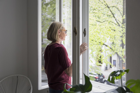 Mature woman at home opening the window stock photo