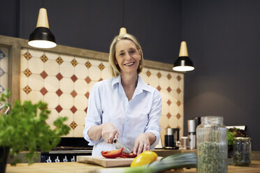 Portrait of smiling mature woman chopping bell pepper in kitchen - RBF05877