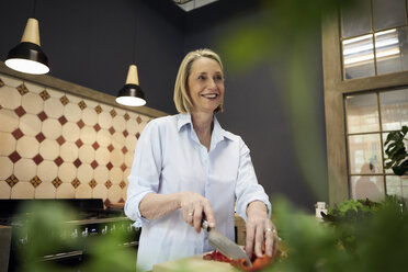 Lächelnde reife Frau hackt Paprika in der Küche - RBF05879