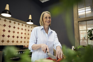 Smiling mature woman chopping bell pepper in kitchen - RBF05879