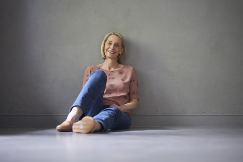 Porträt einer lächelnden reifen Frau, die zu Hause auf dem Boden sitzt, lizenzfreies Stockfoto