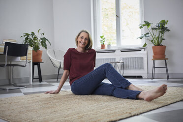 Smiling mature woman sitting on the floor at home - RBF05891