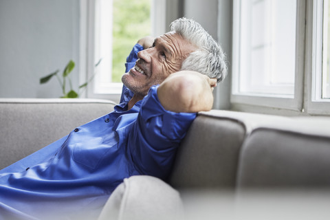 Entspannter reifer Mann sitzt zu Hause auf der Couch, lizenzfreies Stockfoto