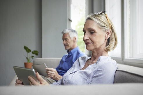 Älteres Paar sitzt zu Hause auf der Couch und benutzt Tablets - RBF05906