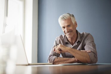 Portrait of confident mature man with laptop and documents at home - RBF05922