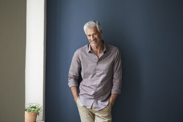 Portrait of confident mature man at home leaning against blue wall - RBF05925