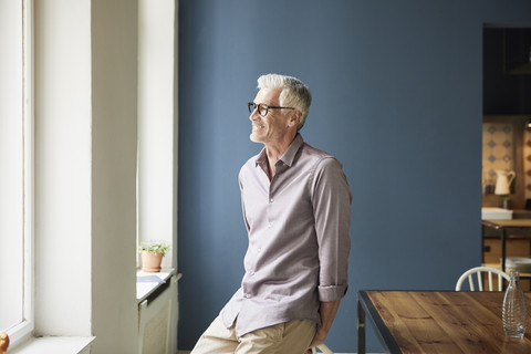 Selbstbewusster reifer Mann zu Hause, der aus dem Fenster schaut, lizenzfreies Stockfoto