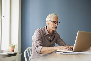 Mature man using laptop on table at home - RBF05927