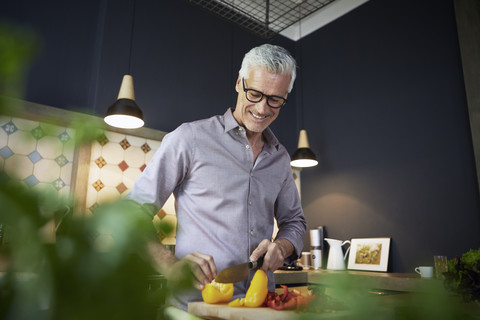 Lächelnder reifer Mann hackt Paprika in der Küche, lizenzfreies Stockfoto