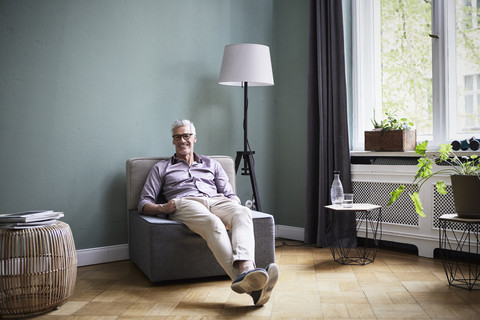 Portrait of smiling mature man sitting on armchair at home stock photo