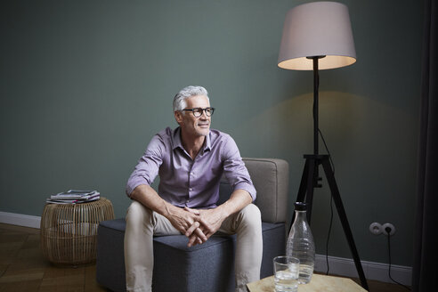Mature man sitting on armchair at home - RBF05935