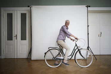 Porträt eines reifen Mannes, der auf einem Fahrrad vor einer Projektionsfläche posiert - RBF05938