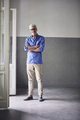 Portrait of smiling mature man standing beside open balcony door at home - RBF05944